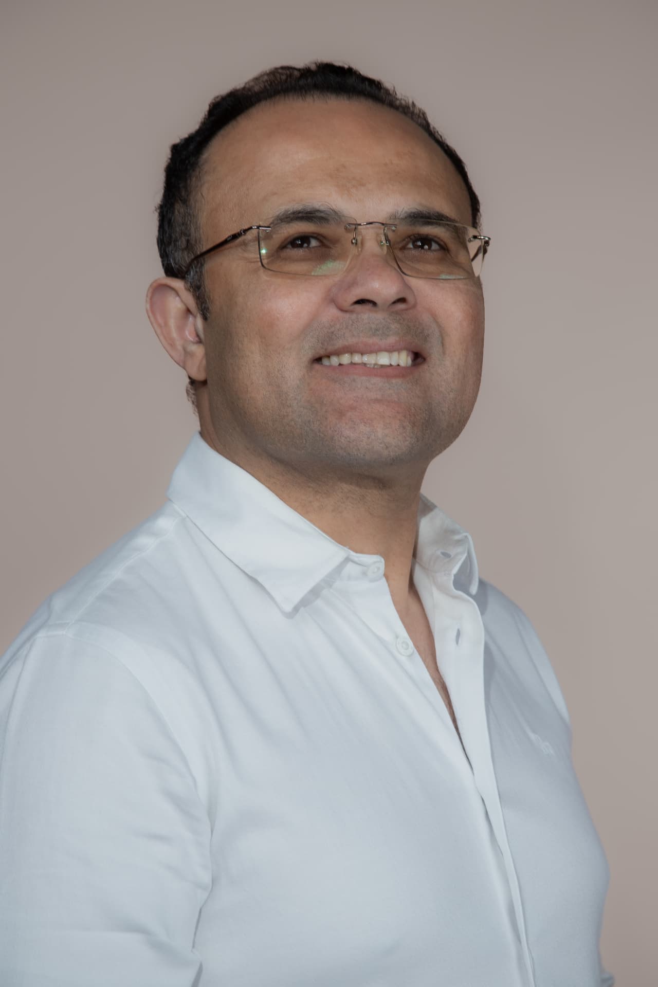 Retrato de Zé Reis, homem de óculos e camisa branca, sorrindo